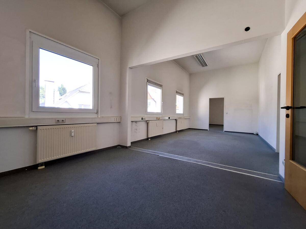 Helles, leeres Büro mit Teppichboden und Fenstern, die viel Tageslicht hereinlassen.