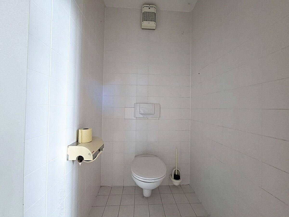 Separate Toilette mit weißen Fliesen, WC und Abluftventilator an der Decke.