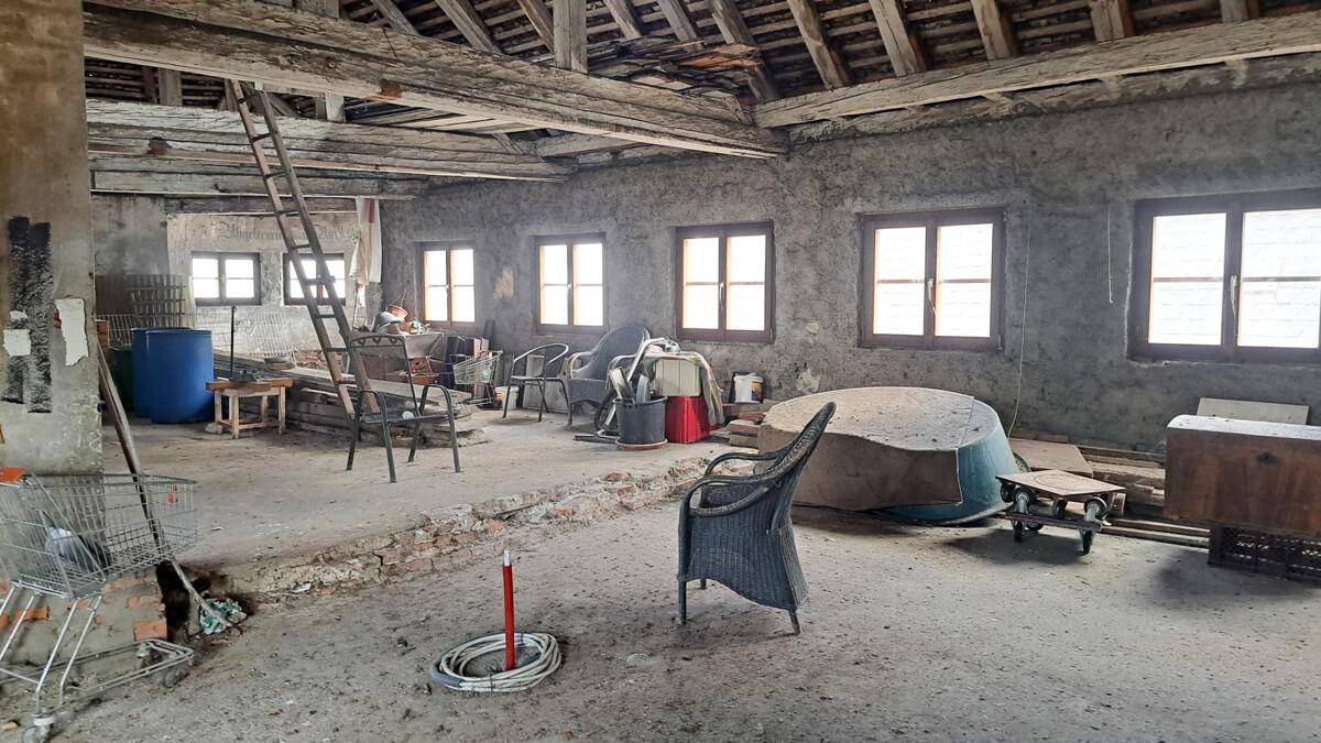 Geräumiger Dachboden mit freiliegenden Holzbalken und mehreren Fenstern, bereit zur Renovierung.