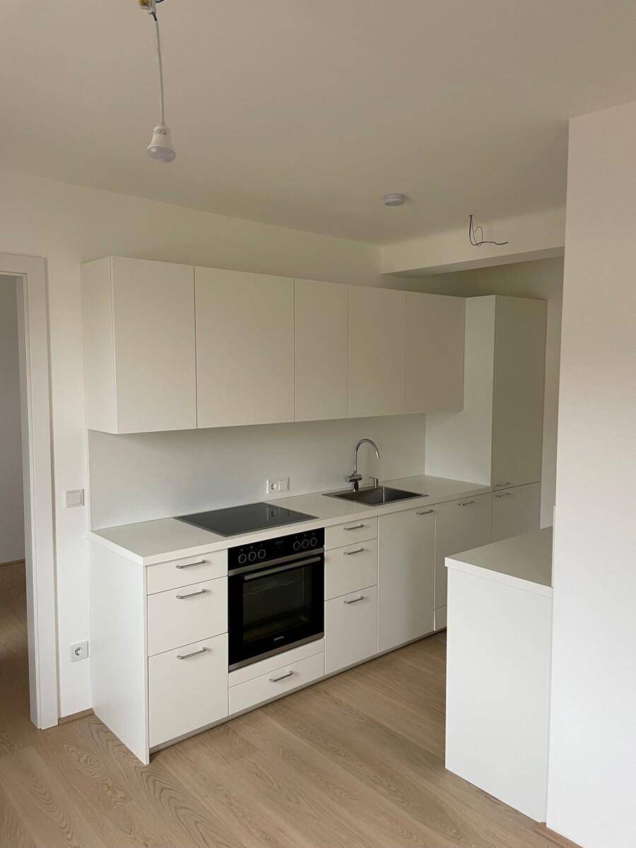Helle Einbauküche mit weißen Schränken, Kochfeld und Backofen.