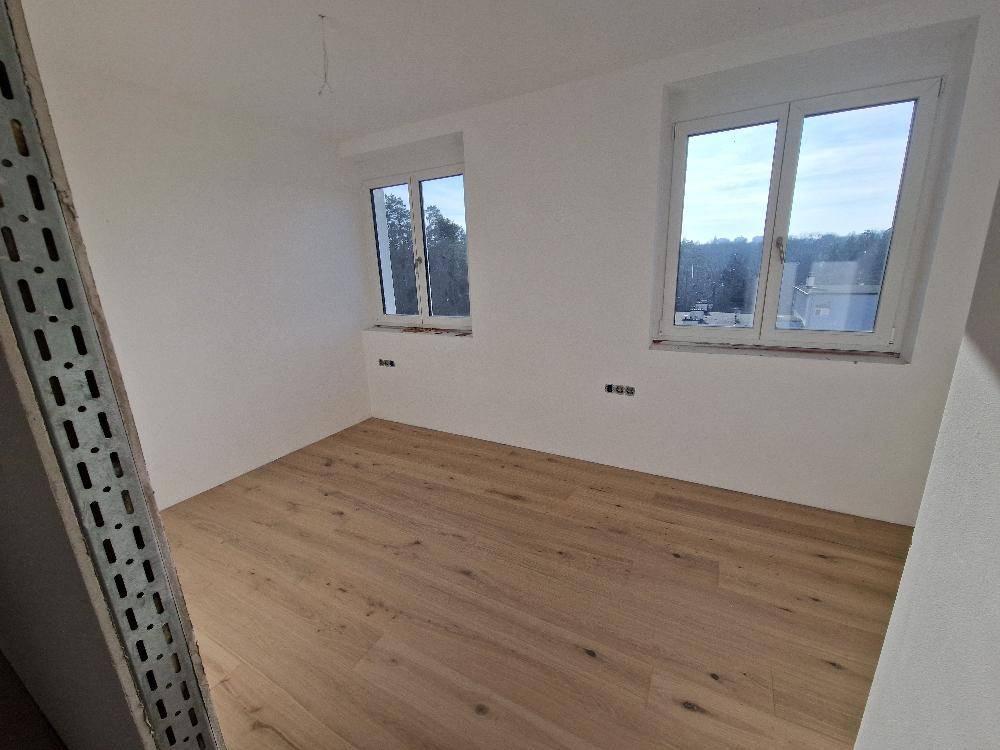 Unmöbliertes Schlafzimmer mit Holzboden und zwei Fenstern, bereit zum Einzug.