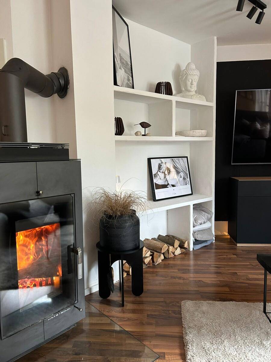 Gemütliches Wohnzimmer mit modernem Kaminofen, Holzregal und dunklem Laminatboden.