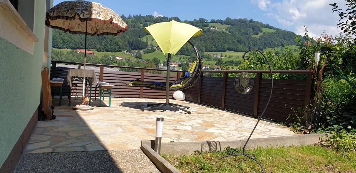 Sonniger Terrassenbereich mit Steinplattenboden, Sonnenschirmen und Bergblick.