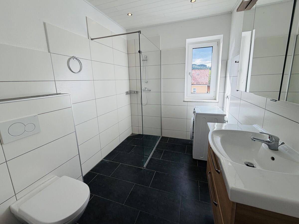 Modernes Badezimmer mit ebenerdiger Dusche, Waschbecken und Waschmaschine.
