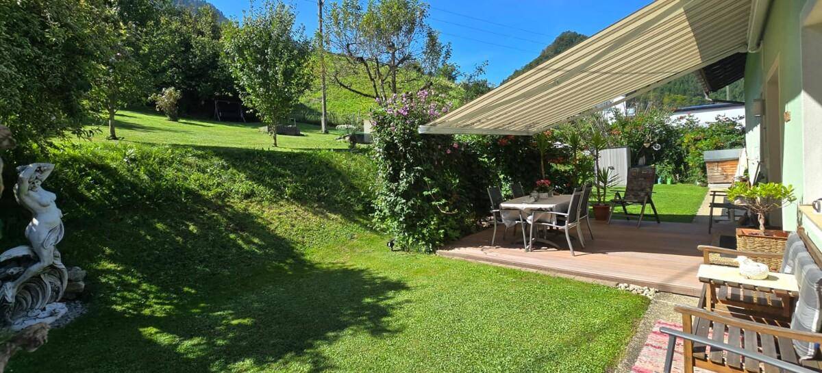 Weitläufiger Garten mit Rasenfläche und einer Holzterrasse mit Markise.