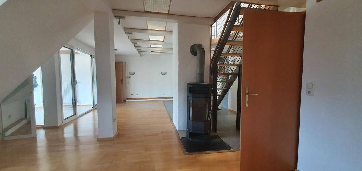 Geräumiger Wohnbereich mit Holzboden, Kaminofen und Zugang zu weiteren Räumen.