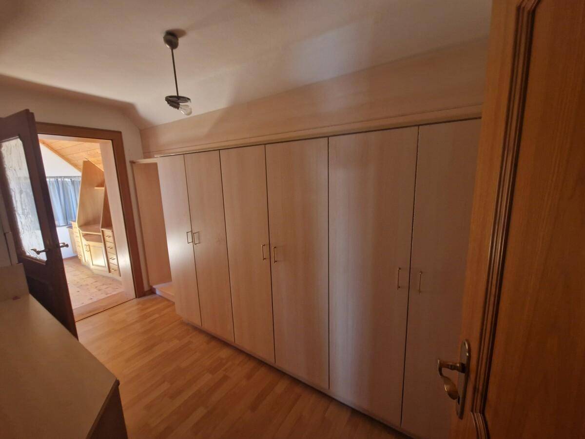 Zimmer mit eingebauten Holzschränken und Zugang zu einem weiteren Raum mit Holzboden.
