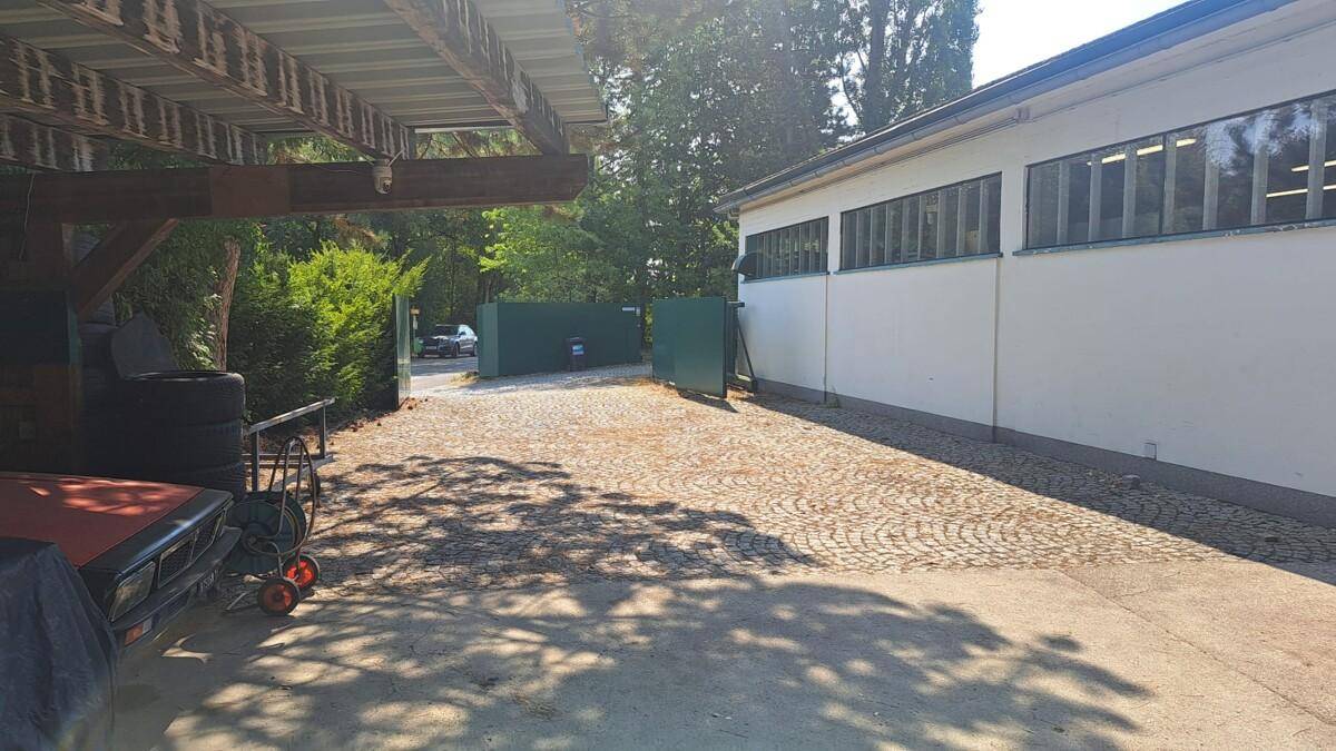 Außenbereich mit gepflasterter Zufahrt, einem Carport und dem Eingang zum Werkstattgelände.