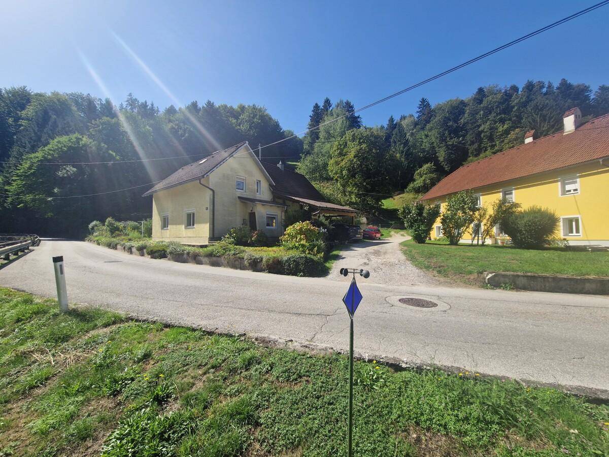 Weitläufige Ansicht des Hauses und der Nachbarschaft mit Straße und grüner Hügellandschaft im Hintergrund.