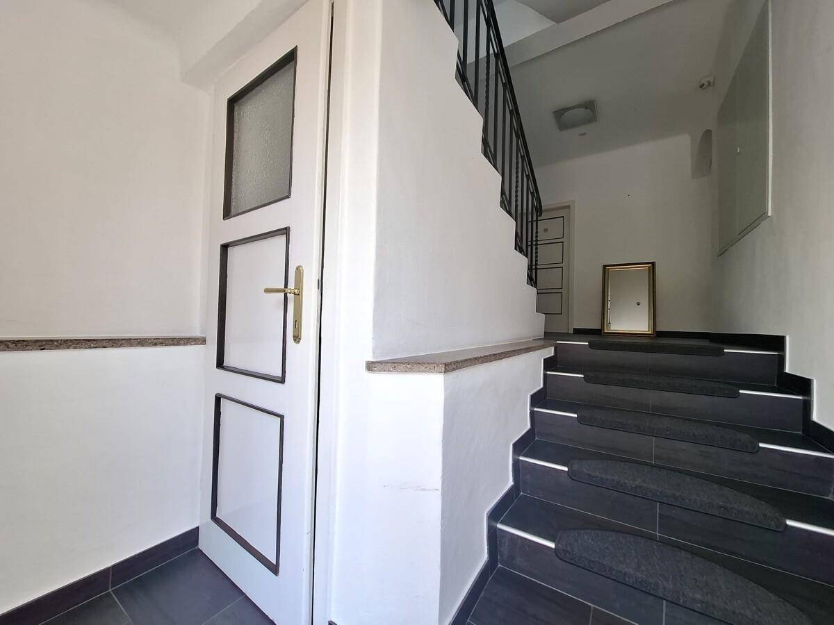 Heller Eingangsbereich mit dunklen Fliesen, Treppe und weißer Tür in modernem Stil.