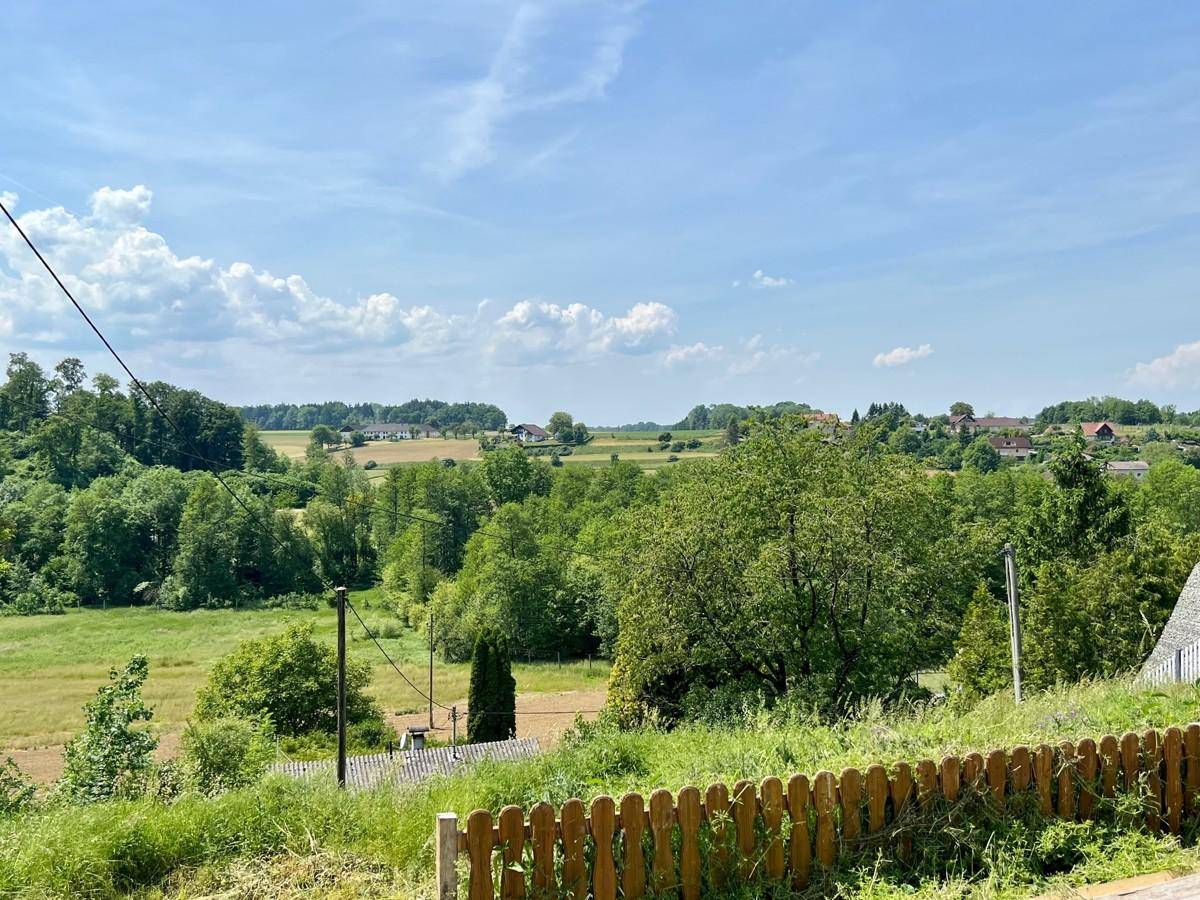 Ländliche Aussicht mit grünen Feldern und bewaldeten Hügeln unter blauem Himmel.