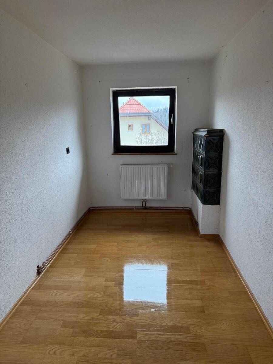 Kleiner Raum mit schwarzem Kachelofen und glänzendem Parkettboden, ideal als Arbeitszimmer.