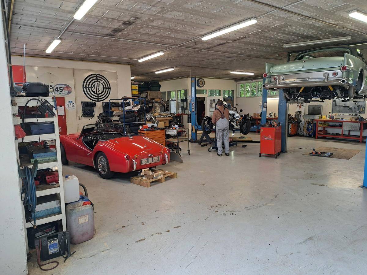 Professionelle Autowerkstatt mit verschiedenen Arbeitsbereichen und historischen Fahrzeugen, gut ausgestattet für Spezialarbeiten.