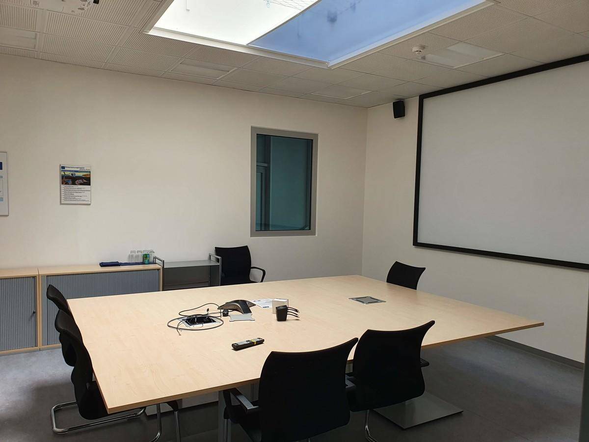 Heller Konferenzraum mit großem Holztisch, bequemen Stühlen, Oberlicht und einem Fenster für Tageslicht.