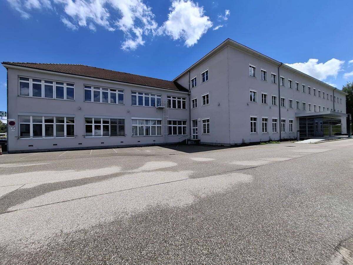 Ansicht des Bürogebäudes von der Seite mit vielen Fenstern und einem großen Parkbereich davor.