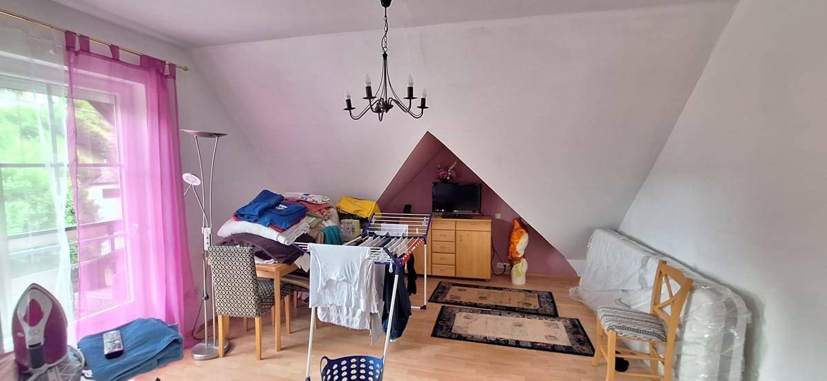 Schlafzimmer im Dachgeschoss mit schrägen Wänden, Holzboden und einem großen Fenster.