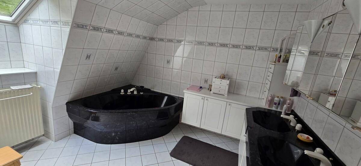 Badezimmer im Dachgeschoss mit Eckbadewanne, Doppelwaschbecken und Fliesenboden.