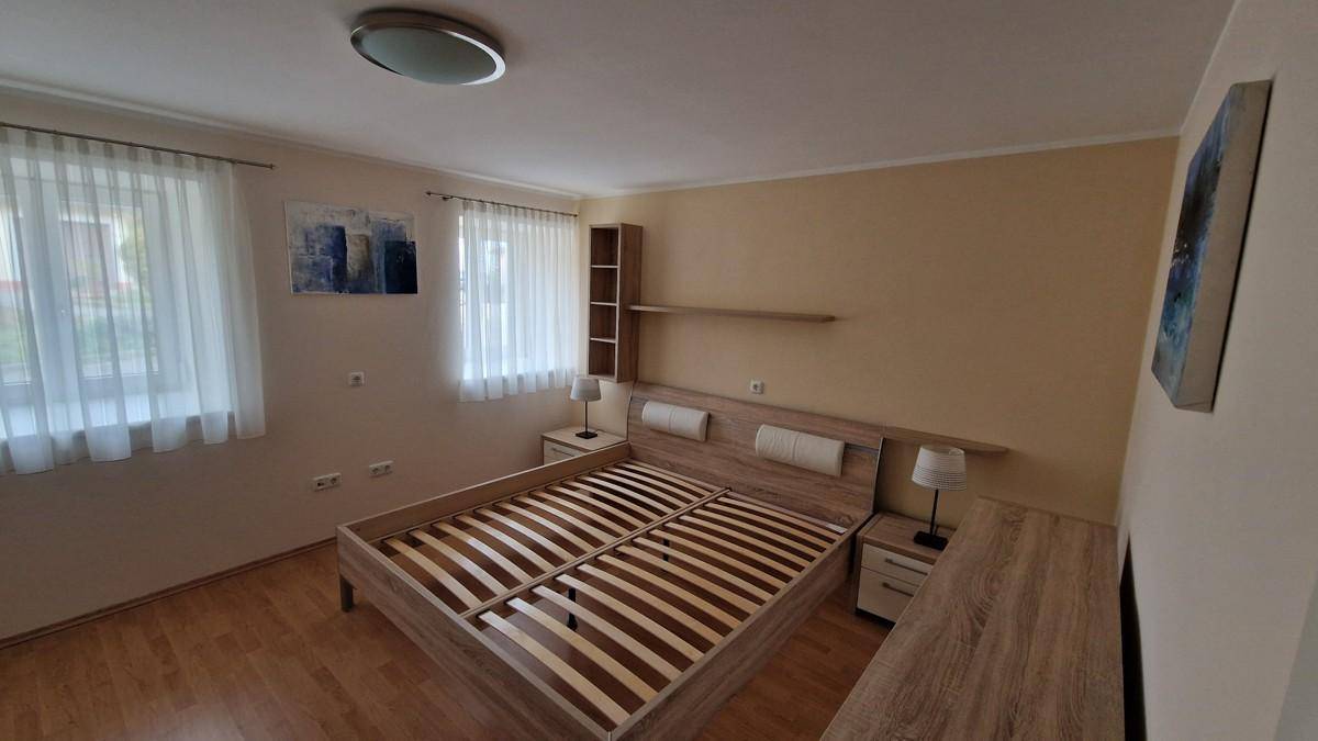 Schlafzimmer mit Doppelbett, Holzboden und zwei Fenstern, die für eine angenehme Helligkeit sorgen.