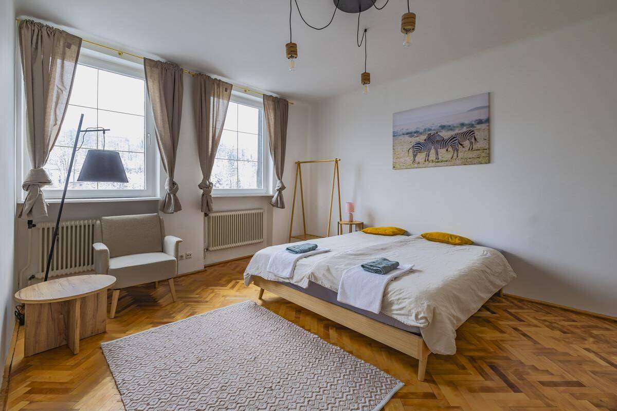 Gemütliches Schlafzimmer mit Parkettboden, Doppelbett und zwei großen Fenstern.
