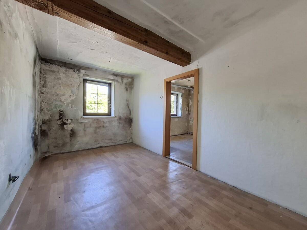 Leerer Raum mit Holzboden, freiliegenden Balken und einem Fenster, bereit zur Renovierung.