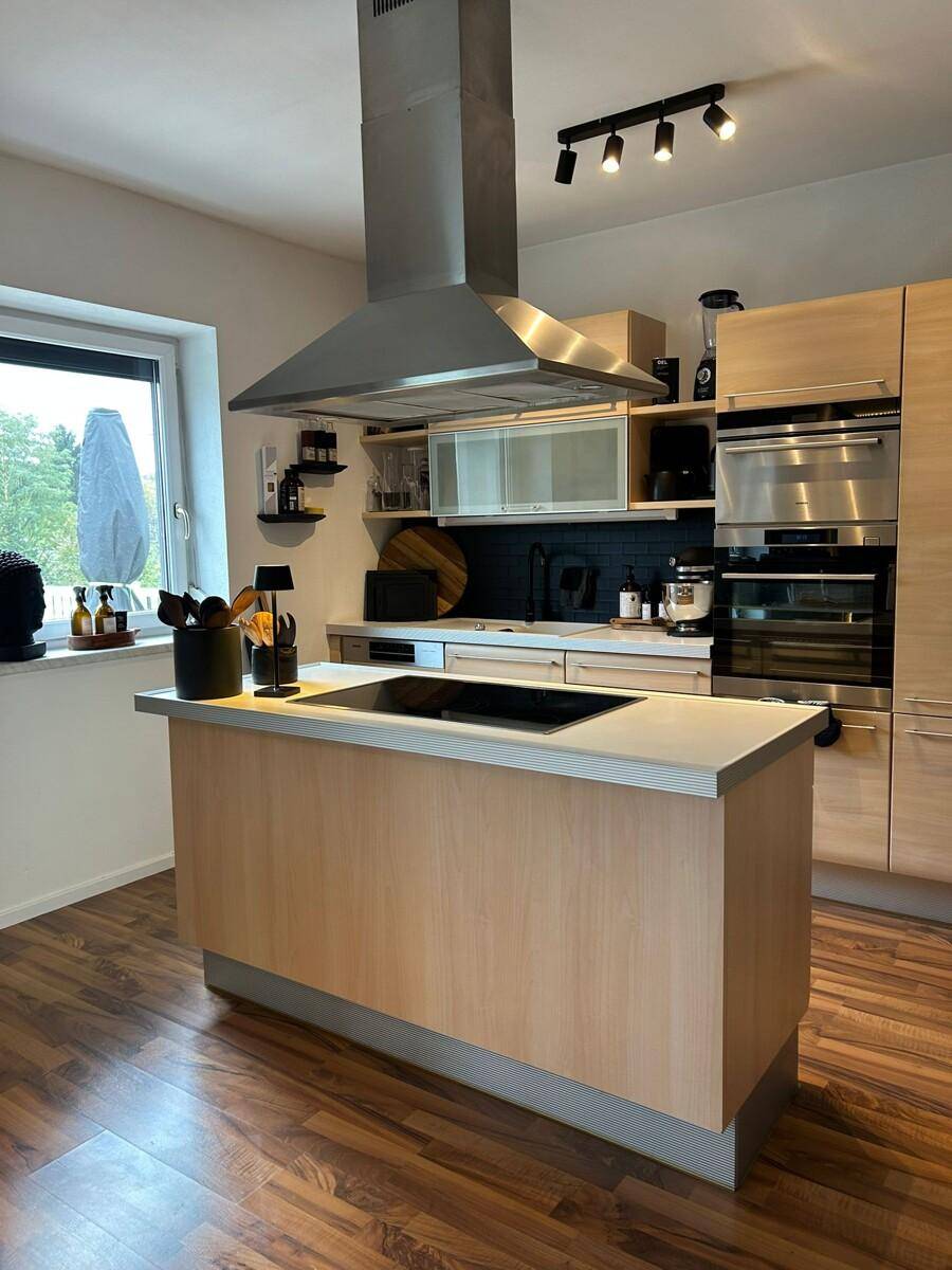 Moderne Küche mit Holzfronten, Kochinsel und Dunstabzugshaube, ausgestattet mit Einbaugeräten.