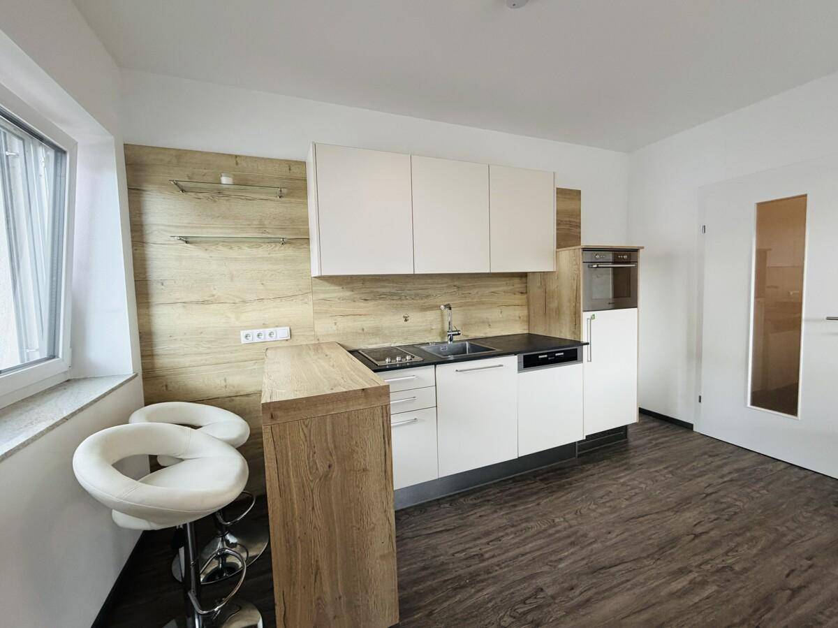 Moderne Küchenzeile mit weißen Schränken, Holzrückwand und Frühstücksbar.