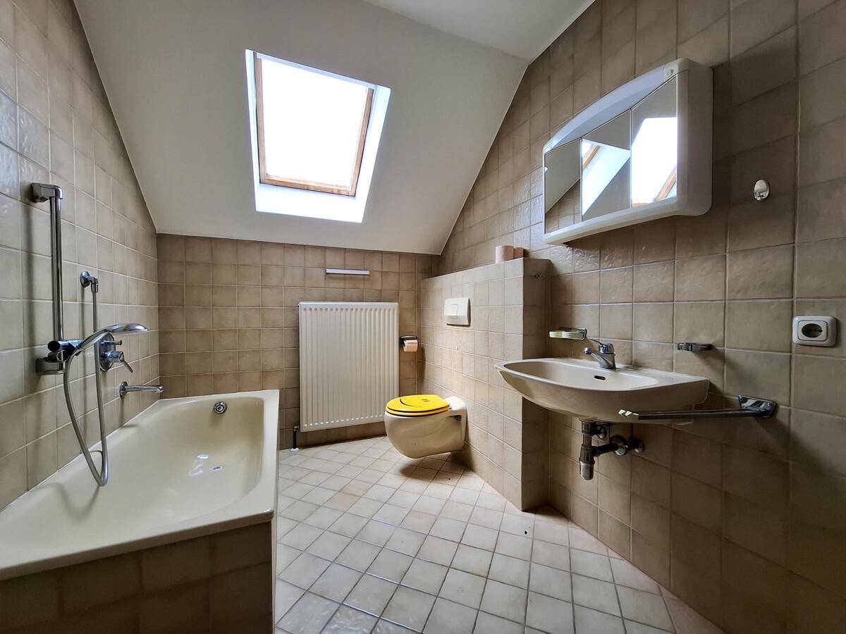 Badezimmer im Dachgeschoss mit Badewanne, Waschbecken und Dachfenster, gefliest in Brauntönen.
