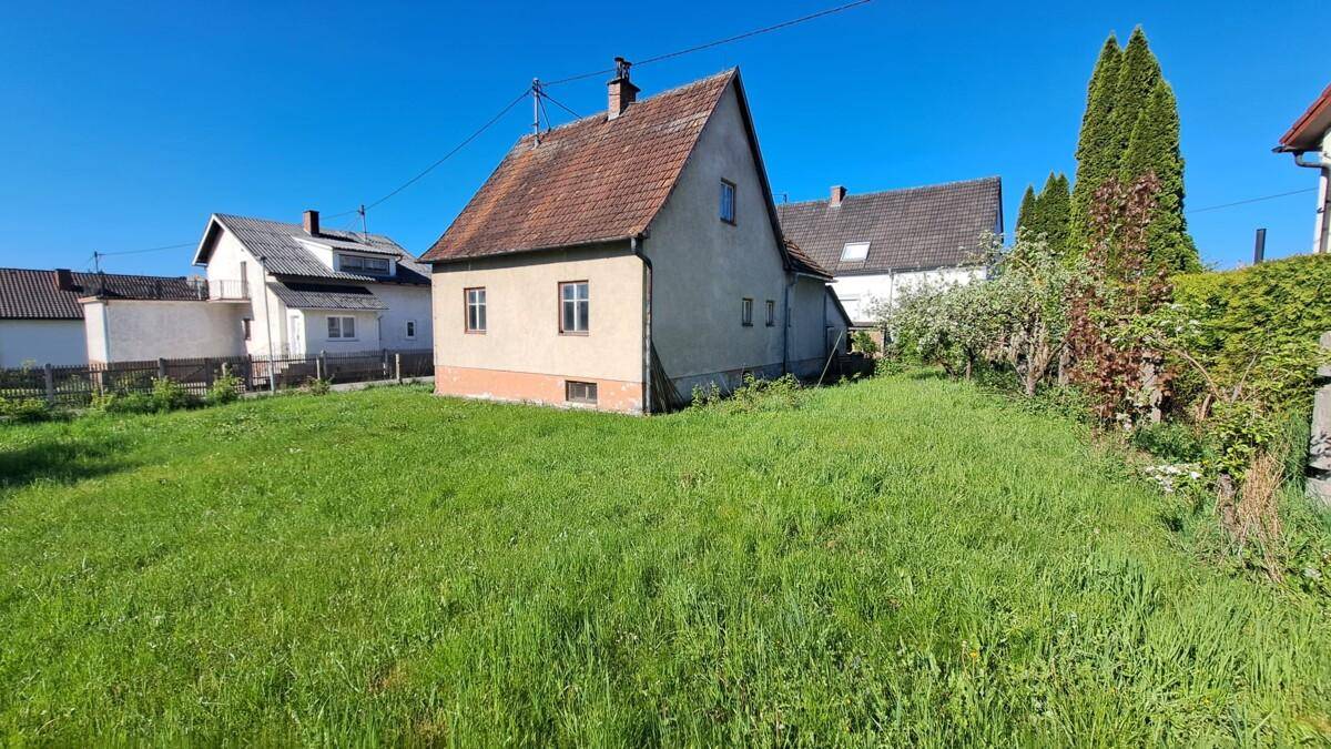 Rückansicht des Hauses mit weitläufigem Rasen und umgebender Natur.