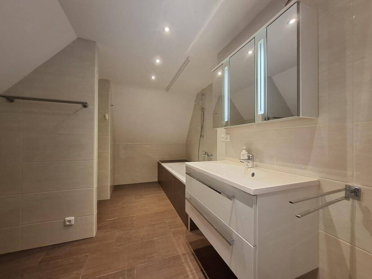 Helles Badezimmer mit Waschtisch, Spiegelschrank und Badewanne unter Dachschräge.