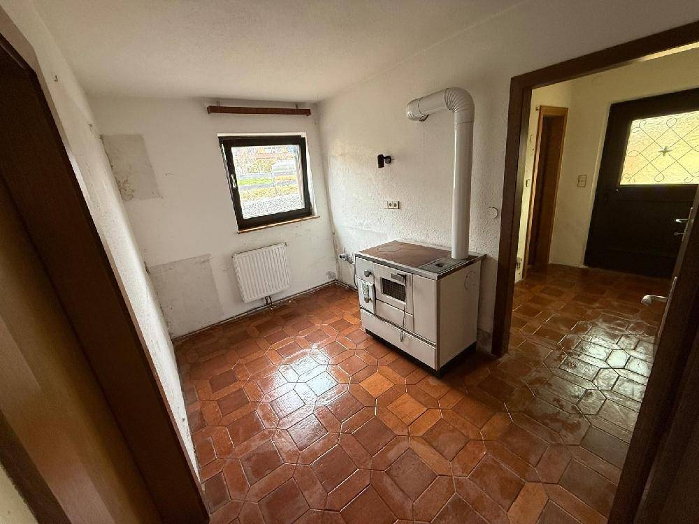 Leerer Raum mit traditionellem Holzofen und gefliestem Boden, bereit für die Kücheneinrichtung.