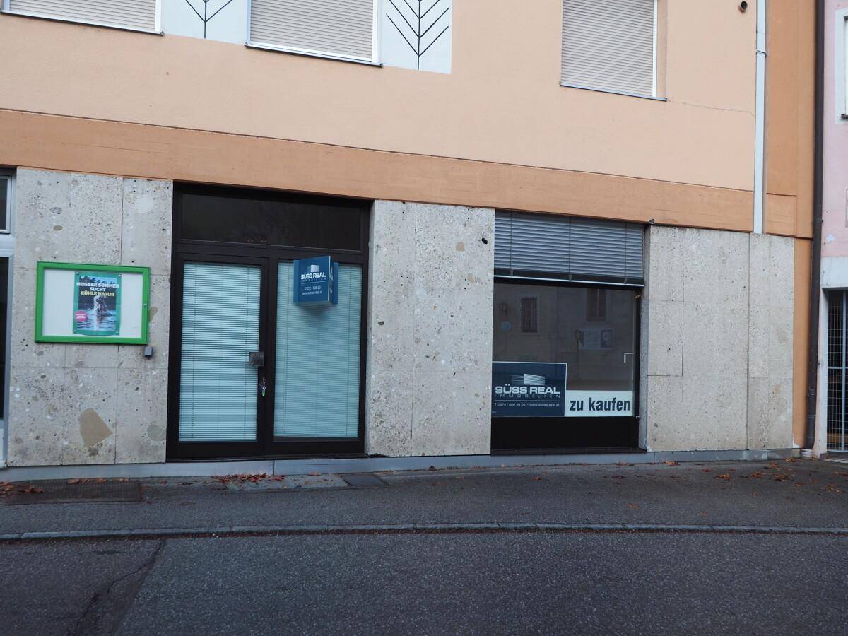 Fassade eines Geschäftsgebäudes im Erdgeschoss mit großen Fenstern und einem Verkaufsschild.