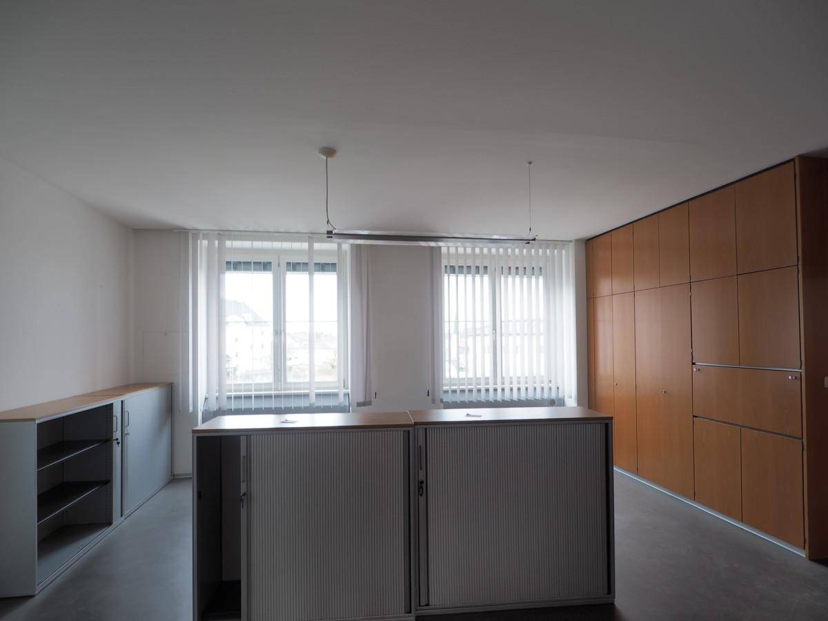 Bürofläche mit großen Fenstern, Holzschränken und Rollcontainern für flexible Arbeitsbereiche.