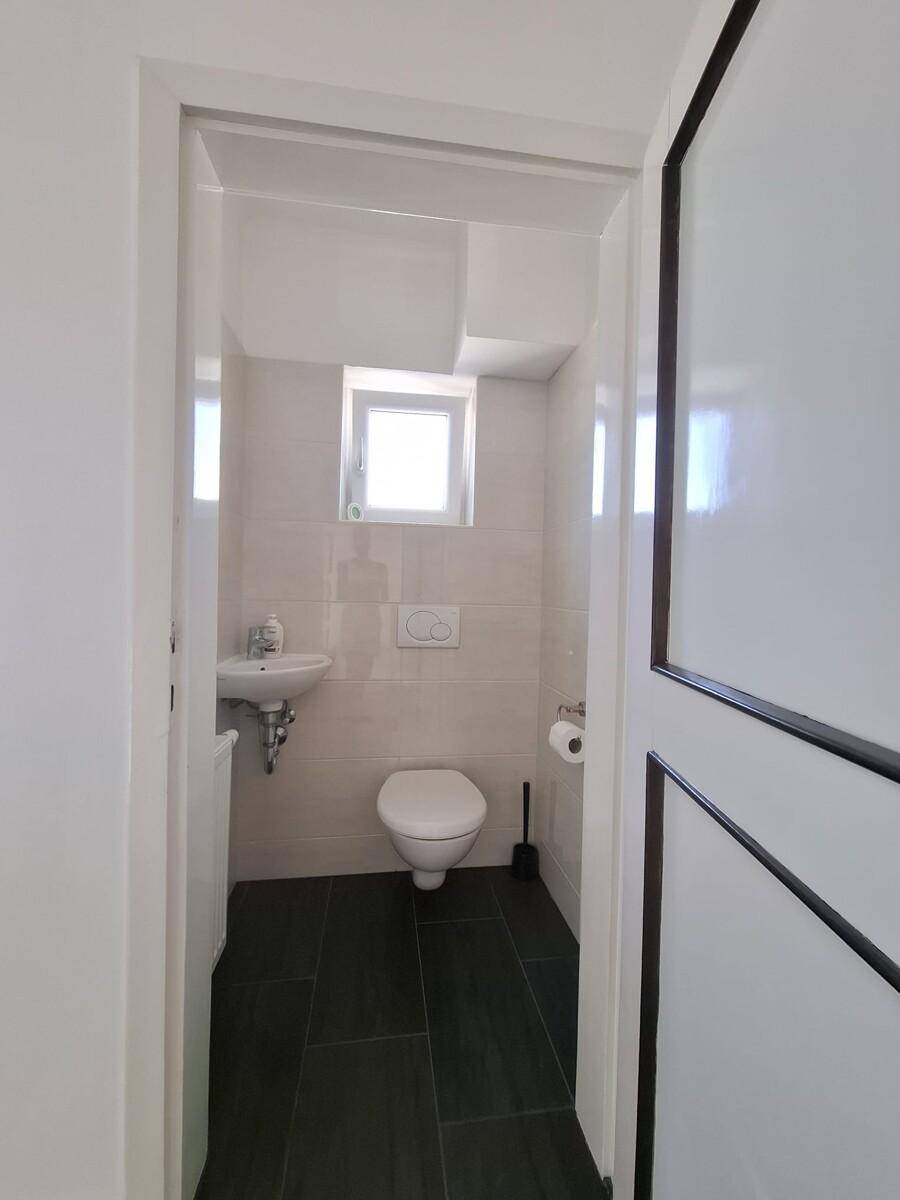 Modernes Gäste-WC mit dunklen Fliesen, wandhängendem WC und kleinem Fenster.