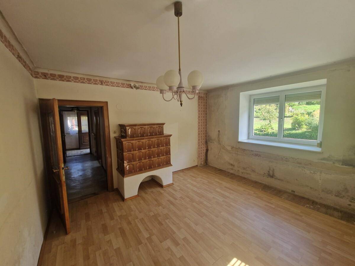 Wohnzimmer mit traditionellem Kachelofen, Holzboden und Fenster mit Blick auf die Landschaft.