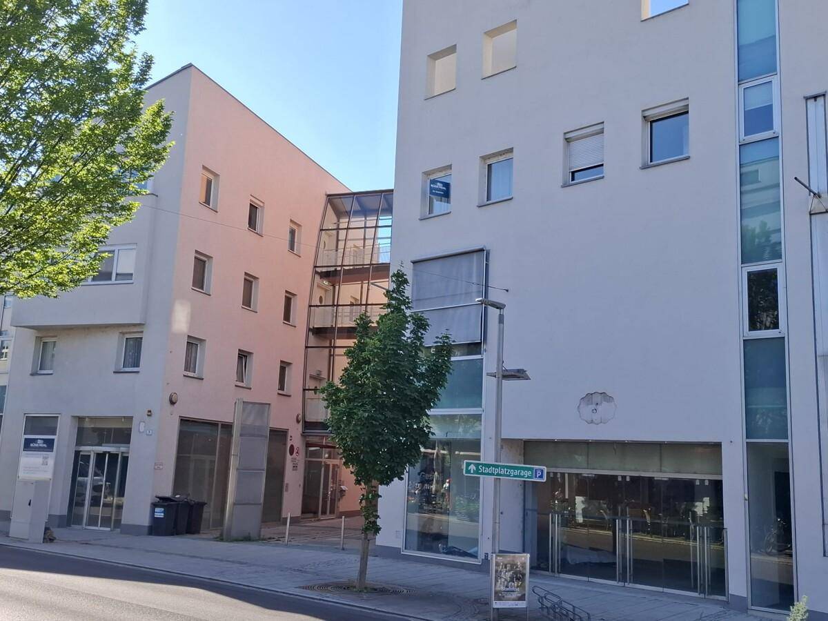 Moderne Gebäudefassade mit vielen Fenstern und einem verglasten Treppenhaus in städtischer Umgebung.