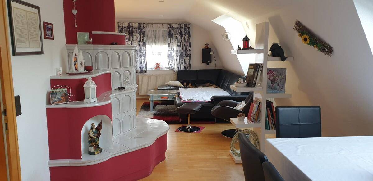 Gemütliches Wohnzimmer im Dachgeschoss mit Kachelofen und Holzboden.