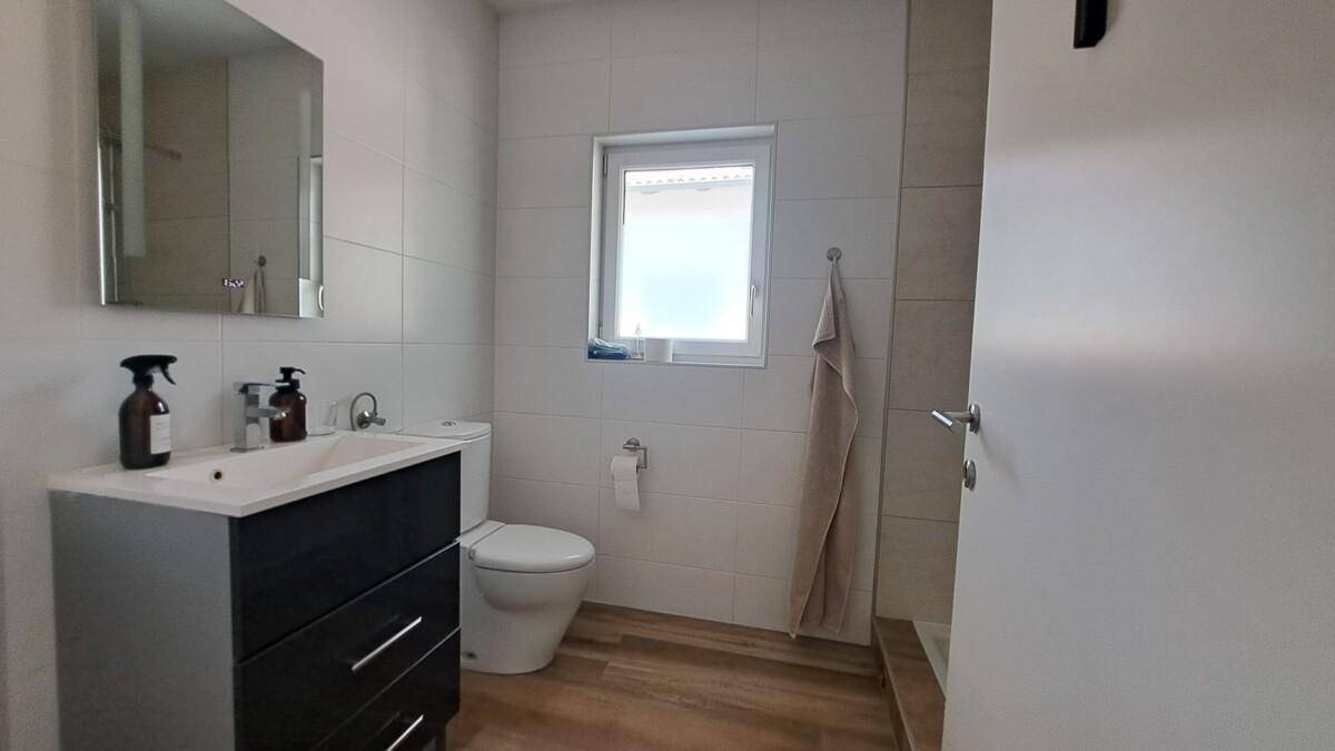 Schlichtes Badezimmer mit Waschtisch, WC und Fenster, ausgestattet mit Holzoptik-Fliesen.