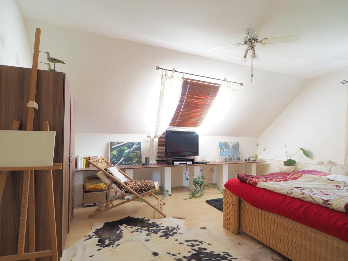 Helles Schlafzimmer im Dachgeschoss mit Dachfenster, Deckenventilator und Holzboden.
