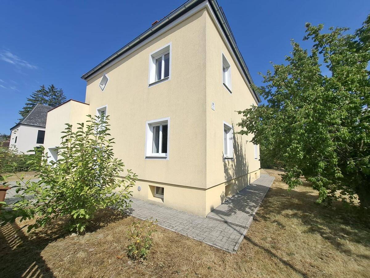 Seitenansicht des Hauses mit mehreren Fenstern und gepflastertem Weg an einem sonnigen Tag.
