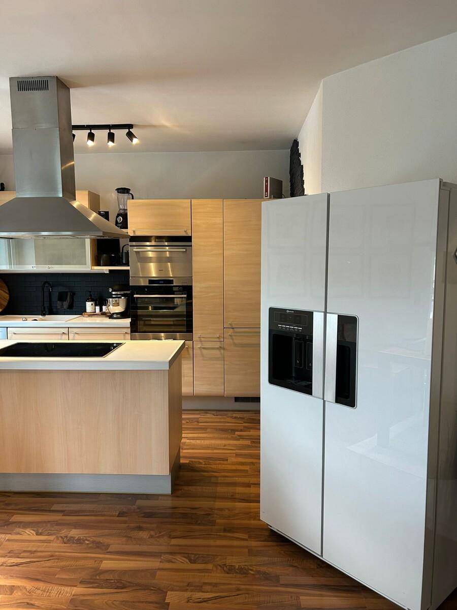 Geräumige Küche mit Holzschränken, Kochinsel und einem modernen Side-by-Side-Kühlschrank.