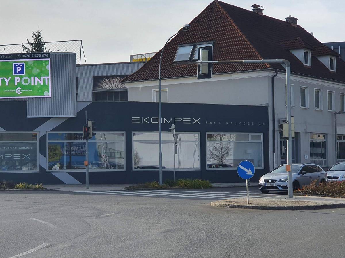 Geschäftsgebäude an einer Kreuzung mit großen Schaufenstern und einem Werbebanner im Hintergrund.