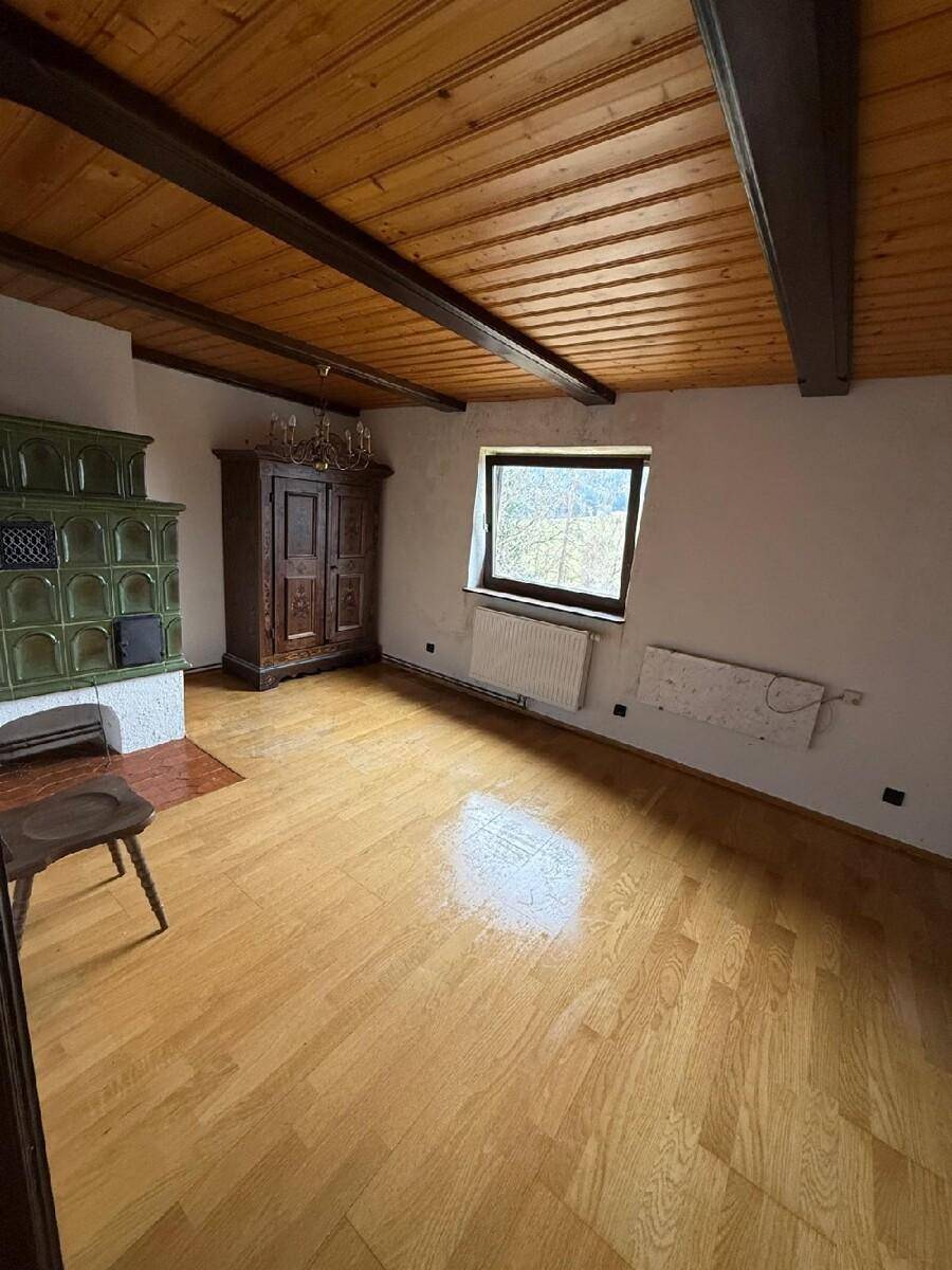 Gemütliches Wohnzimmer mit Holzbalkendecke, grünem Kachelofen und hellem Parkettboden.