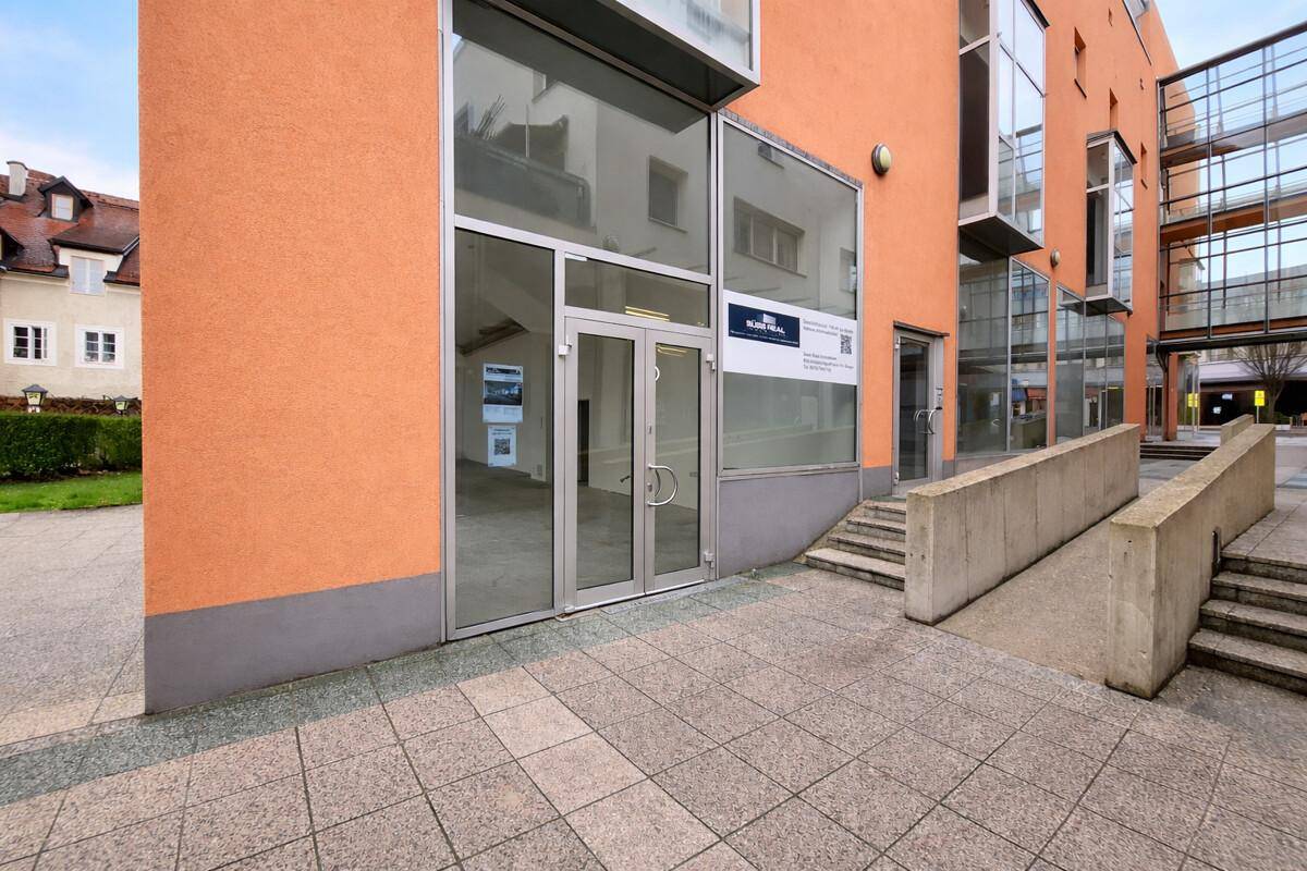 Eingangsbereich eines modernen Gebäudes mit oranger Fassade, Glastüren und Steintreppen.