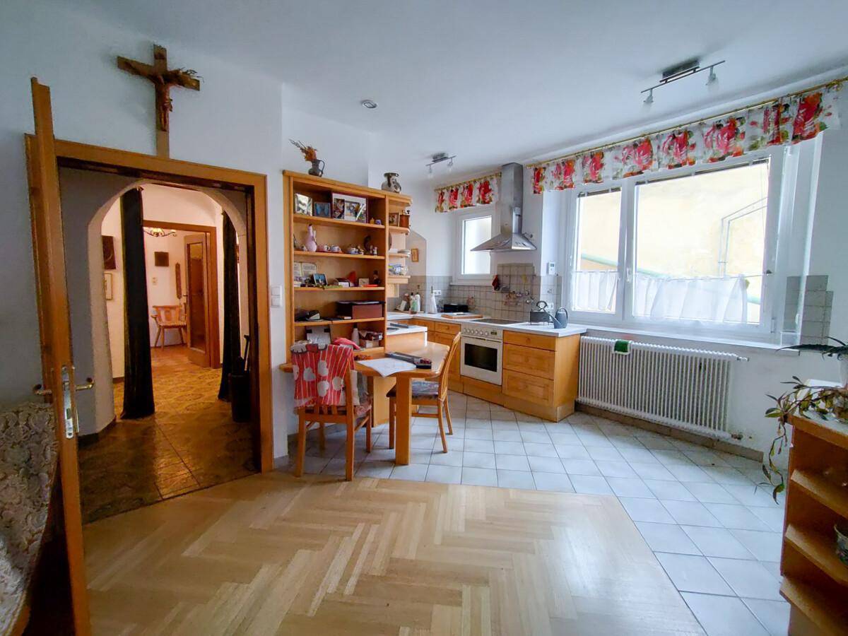 Gemütliche Wohnküche mit Holzeinbauten, Esstisch und Fliesenboden, mit Blick ins Nebenzimmer.
