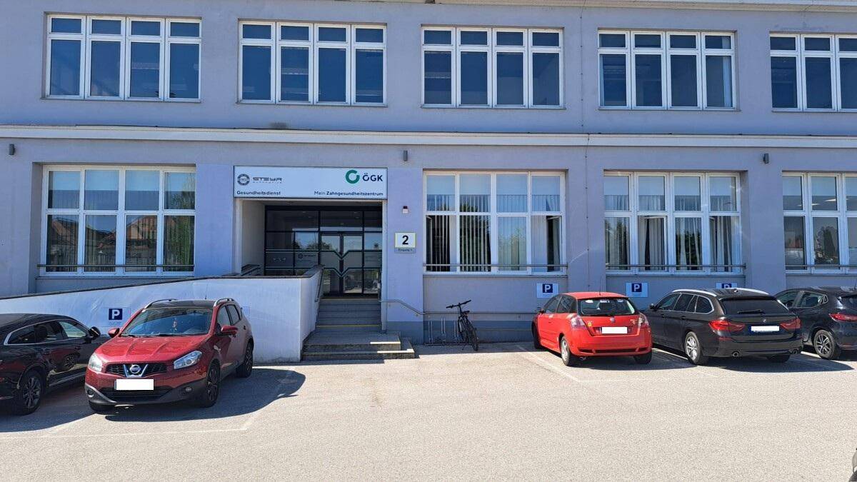 Außenansicht eines modernen Bürogebäudes mit großen Fenstern und mehreren Parkplätzen.