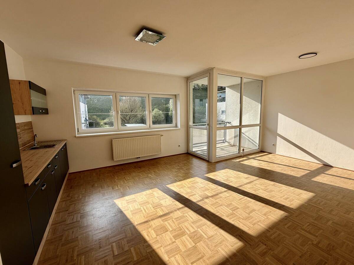 Lichtdurchfluteter Wohnbereich mit Parkettboden und direktem Zugang zum verglasten Balkon.