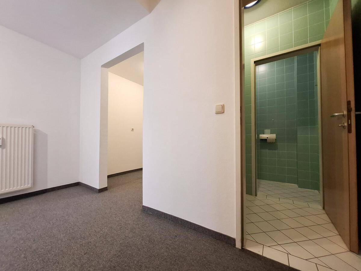 Flur mit grauem Teppichboden und Zugang zu einem Badezimmer mit grünen Fliesen.