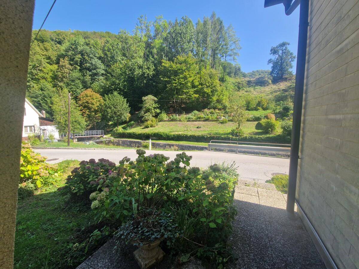 Blick von einem Eingangsbereich auf die Straße und die grüne, bewaldete Hügellandschaft.