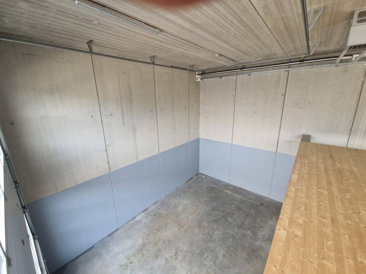 Ecke eines Lagerraums mit Betonwänden, Betonboden und einem Teil der Holz-Zwischenebene.