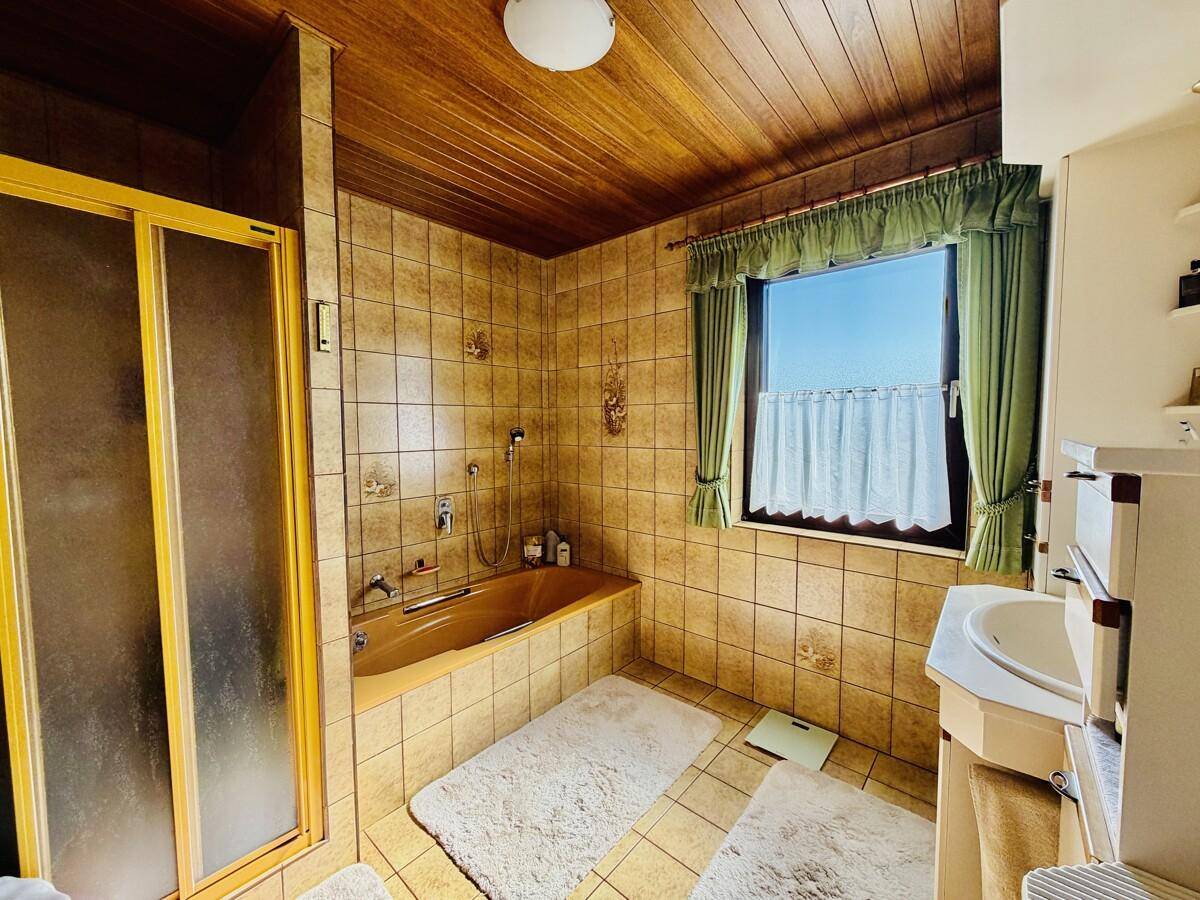 Badezimmer im Stil der 80er Jahre mit braunen Fliesen, Badewanne und Duschkabine.
